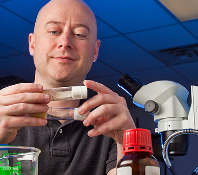 Professor Todd Blankenship examines test tube samples in a research lab.